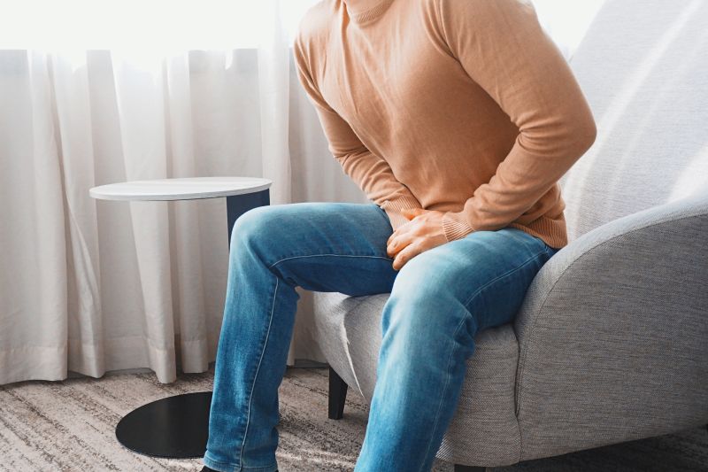Man sitting in a chair holding his groin in pain